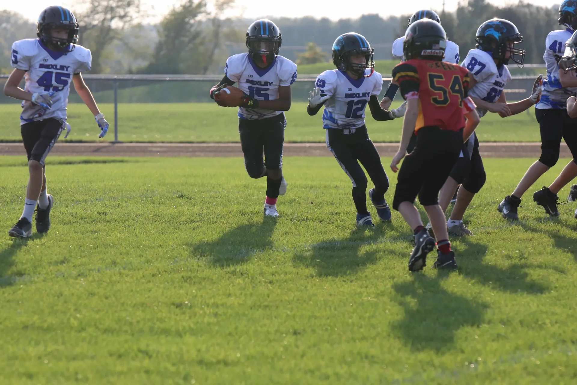 A Bexley ball carrier heads upfield in golden-hour light, the whole play converging behind him.