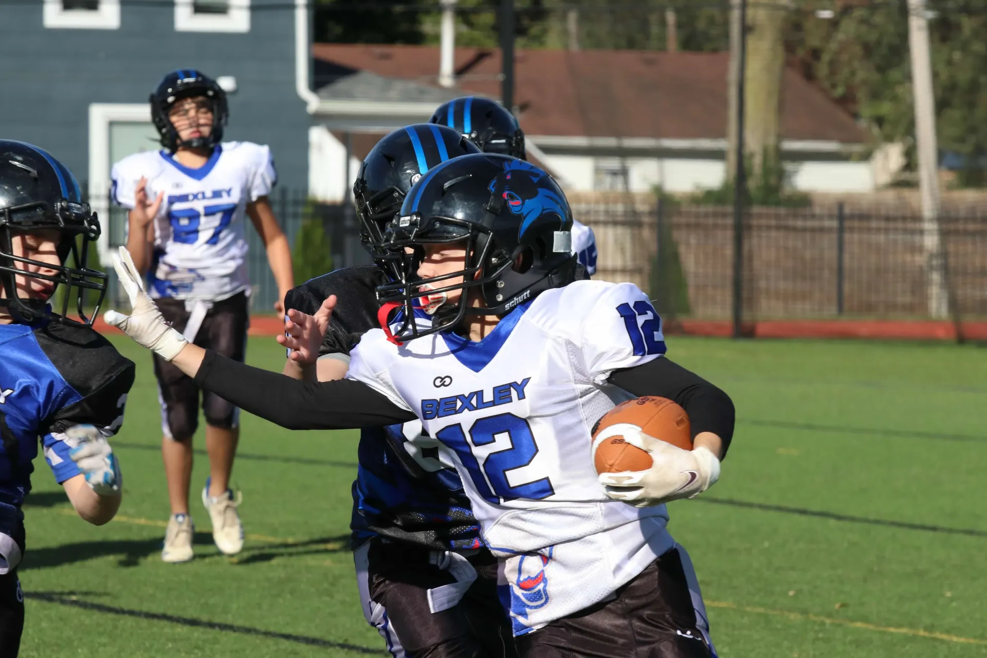 A Bexley runner in white holds off a defender with a stiff-arm.